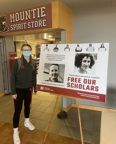 Two students next to a sign that says Free Our Scholars. Poster features photos of two scholars.